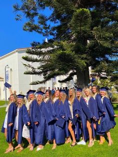 a group of women in graduation gowns posing for a photo on the grass near a church