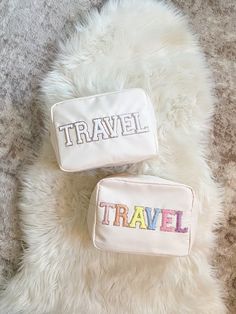 two personalized travel bags sitting on top of a fluffy white rug with the word travel embroidered on it