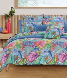 a bed covered in a colorful comforter next to a wooden table with vases on it