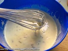 a blue bowl filled with batter and whisk on top of a wooden table