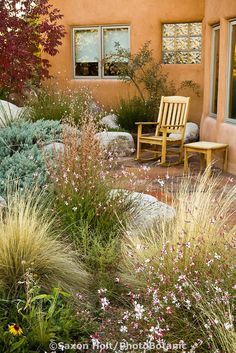 a chair sitting in the middle of a garden next to a house with flowers and plants around it