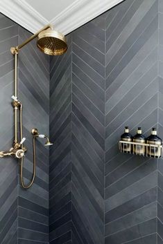 a bathroom with gray herringbone tile and gold shower faucet in the corner