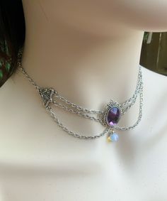 Add a perfect touch of mysterious victorian vampire with this beautiful silver chocker.  The center stone is a lavender faceted glass, set into an antique silver tones bezel. A small moonstone glass bead dangles underneath.  A chain loops on each side, attached it to a filigree connector.  Adjustable, starting at 14 inches and can be worn up to 16 inches. This makes an excellent gift for a loved one or yourself!