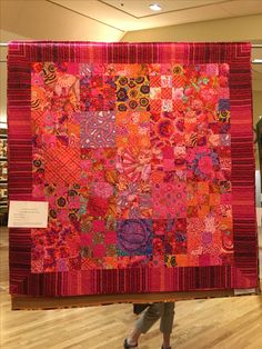 a woman is holding up a colorful quilt