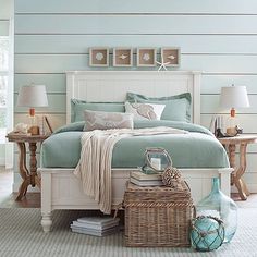 a white bed with blue sheets and pillows in a room next to two lamps on either side of the bed