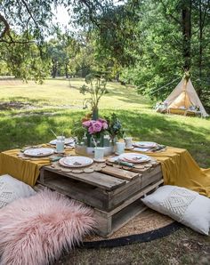 a picnic table set up outside in the grass with pink flowers and plates on it