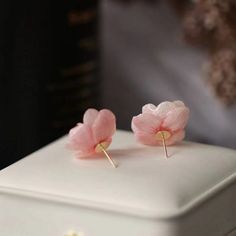 two pink flowers are placed on top of a white box with gold ear pins in it