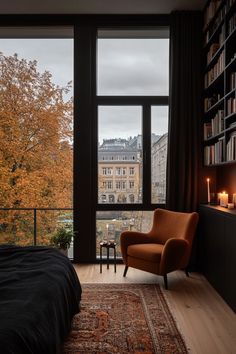 a bedroom with a large window and an orange chair in front of the bed is lit by candles