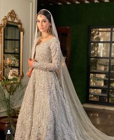 a woman in a white gown and veil standing on a wooden floor with a mirror behind her