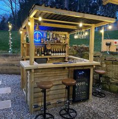 an outdoor bar with stools and lights on the outside wall, in front of a grassy area