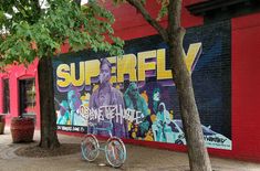 a mural on the side of a building with bicycles parked next to it and trees in front