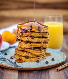 a stack of pancakes on a plate with chocolate chips and orange juice in the background