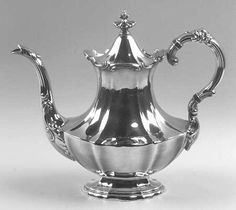 a silver tea pot on a stand with two handles and an ornate design around the top