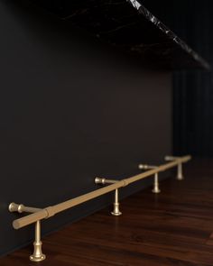 three brass handles on the wall in an empty room with dark walls and wood flooring