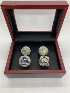 two gold and blue rings sitting in a red box on top of a white table