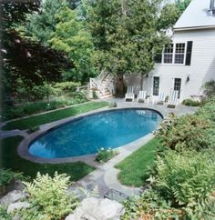 an above ground pool surrounded by lush greenery and rocks in front of a white house