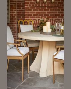 a table with chairs and candles on it in front of a brick wall, surrounded by greenery