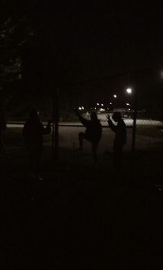 some people are playing frisbee at night in the dark by a chain link fence