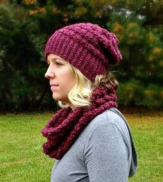 a woman wearing a knitted hat and scarf in the grass with trees in the background