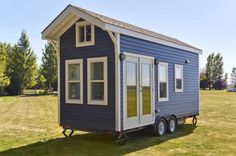 a small blue and white house sitting in the middle of a grass covered field on wheels