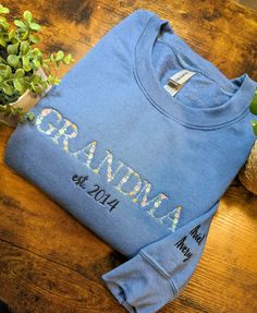 Grandma Floral Sweatshirt This Grandma sweatshirt features a beautiful floral design that adds a touch of femininity to this cozy sweatshirt. It is perfect for both casual outings and lounging around the house. Comes with a personalized sleeve with your grand-kiddo's name as well as a year personalization of when your first grandchild was born! Select options from dropdowns for sweatshirt color, size, and how many names desired for sleeve. 1. Name(s) exactly as you want to appear. (12 char per name.) 2. Year for "est." on front of shirt. 3. Font for sleeve name(s). (Refer to photos.) 4. Thread color for sleeve & "est. year". (Refer to photos.) Welcome to The Threaded Daisy store. Thank you for visiting!  Production & Shipping: Everything is embroidered to order just for you. On average you Blue Embroidered T-shirt For Fall, Embroidered Cotton Short Sleeve Sweatshirt, Blue Cotton Sweatshirt With Floral Embroidery, Ligonier Pa, First Grandchild, Grandma Sweatshirt, Floral Sweatshirt, Embroidered Sweatshirt, Cozy Sweatshirts