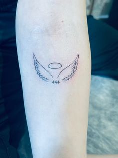 a small tattoo on the leg of a woman's arm with two wings and an oval