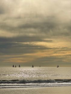 several sailboats are out on the ocean in front of an overcast sky at sunset