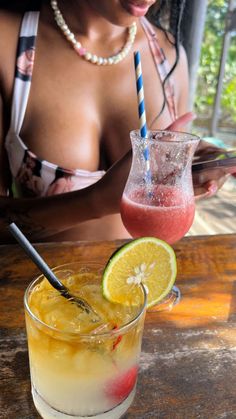 a woman sitting at a table with a drink in front of her and another person holding a cell phone