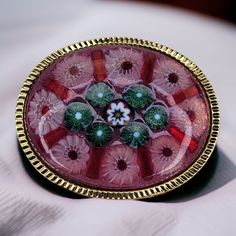 Adorned with an exquisite symphony of colors and intricate patterns, this vintage Italian Millefiori glass brooch is a testament to the enduring legacy of Venetian glassmaking. Crafted by skilled artisans using ancient techniques, the brooch features a mesmerizing array of tiny glass rods fused together, forming a kaleidoscopic patchwork of flowers, stars, and geometric designs. Its smooth, rounded surface shimmers and reflects light, creating a captivating visual display. The brooch is secured with a sturdy pin, allowing it to be elegantly displayed on lapels, jackets, or scarves. The intricate details and vibrant hues of this vintage Millefiori glass brooch evoke a sense of timeless beauty and Italian artistry, making it a cherished collectible and a captivating piece of wearable art. Multicolor Cabochon Brooch For Gift, Multicolor Cabochon Brooch As Gift, Multicolor Cabochon Brooches As Gift, Multicolor Cabochon Brooches For Gifts, Multicolor Cabochon Brooches For Collectors, Victorian Style Multicolor Brooches As Gift, Vintage Multicolor Collectible Brooches, Antique Multicolor Brooch For Gifts, Antique Multicolor Brooches As Gifts