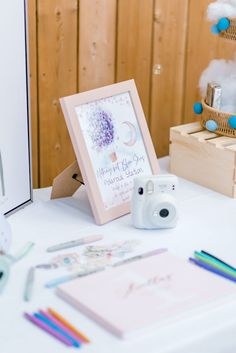 a white table topped with a camera next to a wooden box filled with pens and pencils