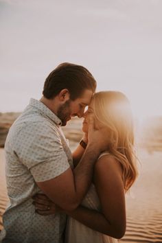 a man and woman standing next to each other in front of the ocean at sunset