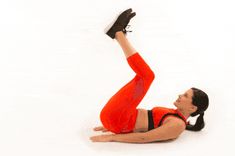 a woman in an orange top and red pants is laying on the floor with her feet up