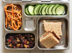 a metal tray filled with different types of food next to cucumbers and pretzels