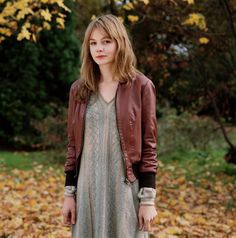 a woman in a dress and leather jacket standing on the ground with leaves all around her