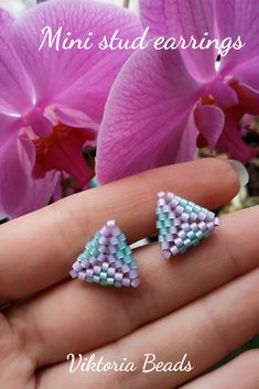 a pair of tiny beaded earrings sitting on top of a persons hand next to pink flowers