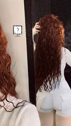 a woman with long red hair is looking at herself in the mirror