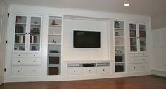 a living room with white bookcases and a flat screen tv mounted on the wall