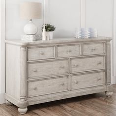 a white dresser sitting on top of a hard wood floor next to a lamp and vase