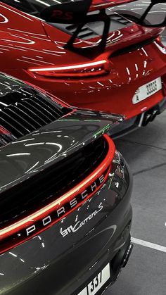 the back end of two red porsches parked in a showroom with other cars