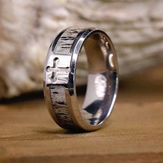 a silver ring with a cross on it sitting on top of a piece of wood