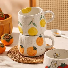 two mugs with fruit painted on them are sitting on a wicker place mat