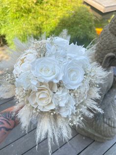 a bride's bouquet with white flowers and feathers is sitting on the ground next to an elephant