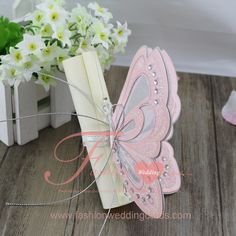 a card with a butterfly on it sitting next to flowers and a vase filled with white flowers