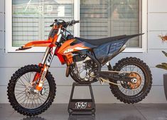 an orange and black dirt bike parked on top of a stand in front of a building