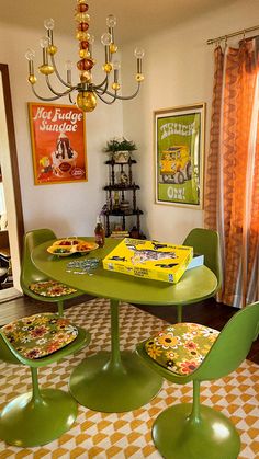 a green table with four chairs and a yellow box sitting on top of it in front of a chandelier