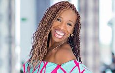 a woman with dreadlocks smiling at the camera while wearing a blue and pink top