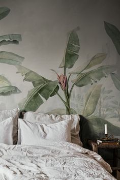 a bed with white linens and green leaves painted on the wall behind it, next to a night stand