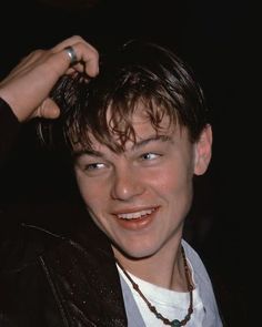 a close up of a person wearing a leather jacket and smiling at the camera with one hand on his head