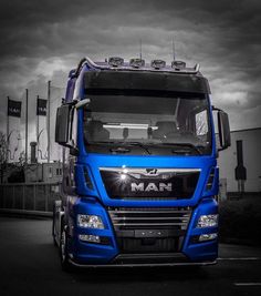 a blue truck parked in front of a building on a cloudy day with dark clouds