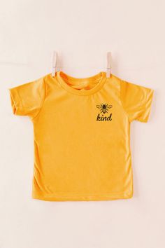 You are sure to be the trendiest mom out there when you wear our adorable neutral hued Shift Tee featuring soft lightweight material, a high rounded neckline, short loose sleeves and a relaxed silhouette that falls into a straight neckline! Pair this with your kiddos for the perfect day out! 100% Cotton This is a Specialty Item and is NOT returnable. This item is made to order and does take additional time to process.Materials may have natural variations Colors may vary from different viewing de Gold T-shirt With Letter Print For Summer, Spring Gold Graphic Print T-shirt, Gold Letter Print Top For Summer, Gold Letter Print Tops For Summer, Yellow Short Sleeve T-shirt For Family Matching, Gold Graphic Tee Tops For Summer, Relaxed Fit Gold Cotton Top, Trendy Gold Cotton T-shirt, Gold Cotton Top With Relaxed Fit